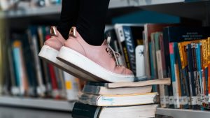 Psychoanalytic, Creative Curiosity and Constructive Skepticism Thought Piece. A person standing on books in library only showing lower legs and floor