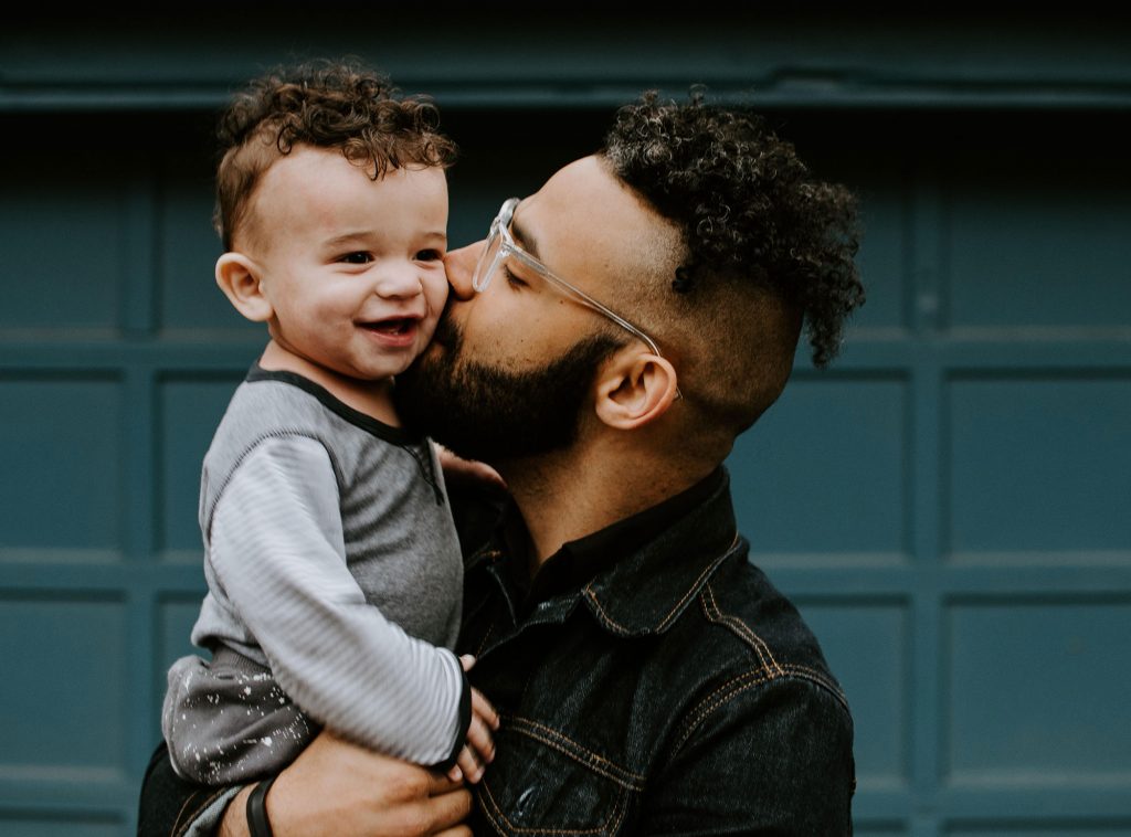 A photo of a father kissing the cheek of his young child