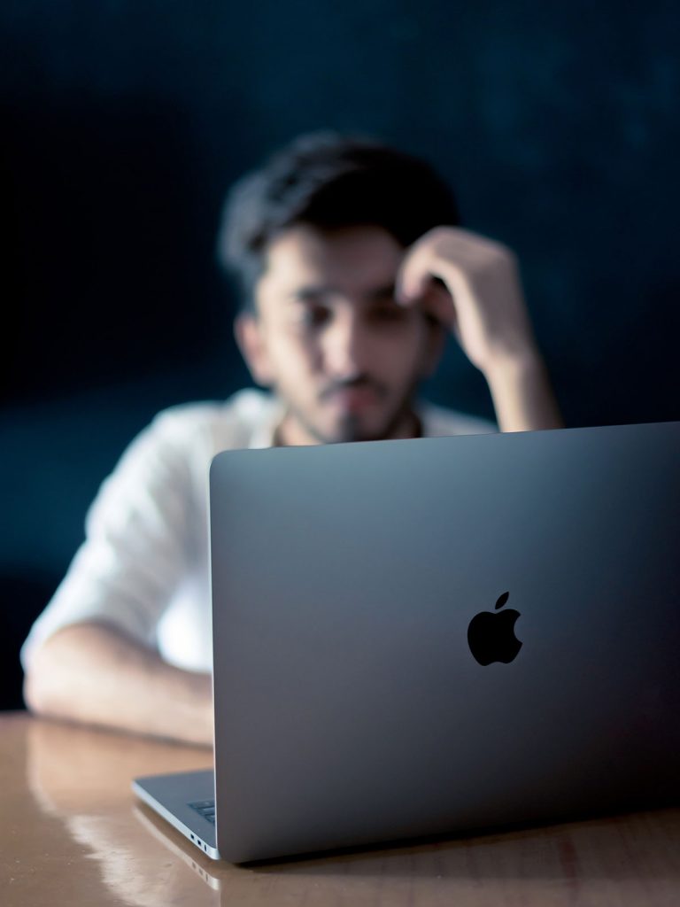 A photo of a blurred man's face sat behind a laptop