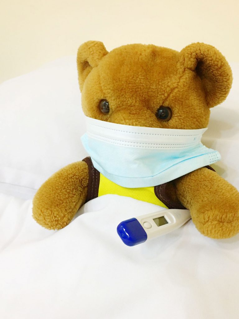 A photo of a teddy wearing a mask holding a thermometer