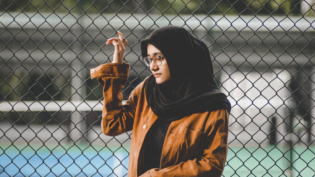A photo of a girl in a hijab holding onto a fence in thought