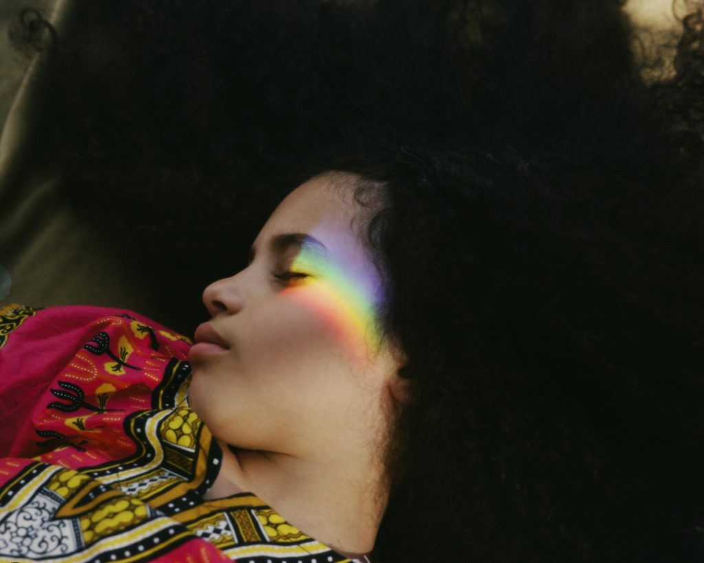 A photo of a girl with eyes closed and rainbow reflection on face